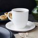 A Villeroy & Boch white porcelain mug of coffee on a saucer next to a pastry.