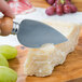 A person using a Franmara stainless steel hard cheese knife to cut a piece of cheese.