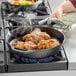 A Choice pre-seasoned cast iron skillet with fried chicken cooking on a stove.