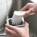 A person washing a vegetable cutter brush on a counter in a home kitchen.