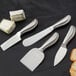 An American Metalcraft stainless steel soft cheese spreader next to a piece of cheese.