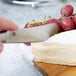 A person using an American Metalcraft stainless steel soft cheese spreader to cut cheese.