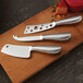 An American Metalcraft stainless steel hard cheese cleaver with holes in the blade on a cutting board with cheese.