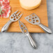 A Franmara stainless steel cheese knife and fork set on a cutting board with cheese.