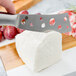 An American Metalcraft stainless steel cheese knife cutting white cheese on a block.