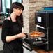 A woman wearing a black apron putting food into a Merrychef eikon e2s high-speed oven.