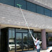 A man using an Unger OptiLoc telescopic pole to clean the outside of a building.
