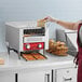 A woman using an Avantco conveyor toaster to make toast on a counter in a professional kitchen.