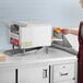 A woman using an Avantco conveyor toaster to make toast in a kitchen.