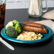 A Jacksonville Jaguars paper dinner plate with a sausage and broccoli on a table with white plastic utensils.
