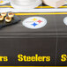 A table with a Pittsburgh Steelers plastic table cover with yellow and white logos on it with small food items.