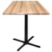 A Holland Bar Stool natural wood table with a black cross base.