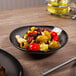 A Reserve by Libbey Pebblebrook obsidian porcelain bowl filled with olives and artichokes on a table.