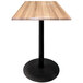 A Holland Bar Stool outdoor table with a natural wood square top and a black round base.