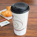 A Solo Symphony foam coffee cup with a black lid on a table with a croissant.
