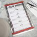 A Menu Solutions Alumitique menu board with red bands on a table with silverware and a white napkin.