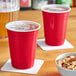 Two red Choice plastic cups filled with beer on a table with a bowl of mixed nuts.