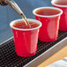 A close-up of a red Choice plastic shot cup with brown liquid being poured into it.