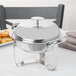 A round silver stainless steel chafing dish with a lid on a table.