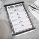 An Alumitique menu board with black bands on a table with a fork and knife.