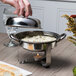 A person using a Libbey stainless steel chafing dish to serve food.
