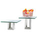 A Rosseto clear tempered glass riser shelf on a glass table with vegetables on top.