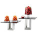 A black square acrylic riser shelf with glass containers of fruit on it.