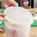 A person using a measuring cup to fill a Choice translucent polypropylene container with a lid.