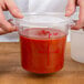A person's hand opening a Choice clear polycarbonate food storage container lid on a container of sauce.
