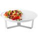A Rosseto white melamine round tray with a plate of food on a 3-leg silver stand.