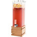 A Rosseto clear acrylic beverage dispenser with a bamboo base filled with red liquid and fruit.