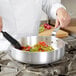 A chef cooking food in a Vollrath Wear-Ever saute pan.