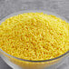 A bowl of Yellow Sprinkles on a gray surface.