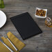 A black Menu Solutions wood menu board on a wood table with a plate and silverware.