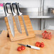 A Mercer Culinary Millennia® knife set on a bamboo magnetic board with white handles next to tomatoes.