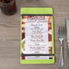 A Menu Solutions wood menu board with lime rubber bands on a table with a fork and knife.