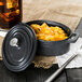 A black Libbey mini cast iron oval dutch oven with food in it and a lid on a table.