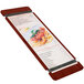 A Menu Solutions mahogany wood menu board with rubber bands on a table holding a menu.
