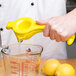 A hand holding a Tablecraft lemon juicer squeezing a lemon into a bowl.