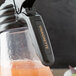 A Tablecraft black polypropylene dispenser tag with orange "Vinaigrette" print on a juice bar counter.