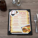 A Menu Solutions wood menu board on a table with a fork and knife on it.