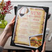 A person holding a Menu Solutions wood menu board with a picture corner on a table in a farm-to-table restaurant.