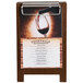 A Menu Solutions walnut wood sandwich menu board tent on a table with a glass of red wine.