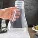 A hand holding a Tablecraft Tritan clear plastic dispenser bottle over a plate of food.
