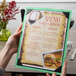 A hand holding a Menu Solutions washed teal wood menu board with picture corners.