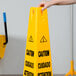 A person's arm holding a yellow Rubbermaid "Caution" cone sign.