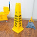 A yellow Rubbermaid wet floor cone sign with "Caution" in multiple languages on a wood floor with a mop.