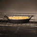A pan of food in an American Metalcraft cast iron oval casserole dish in an oven.