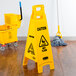 A yellow Rubbermaid wet floor sign next to a mop and a yellow bucket.