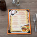 A Menu Solutions wood menu board on a table with a menu and picture corners.